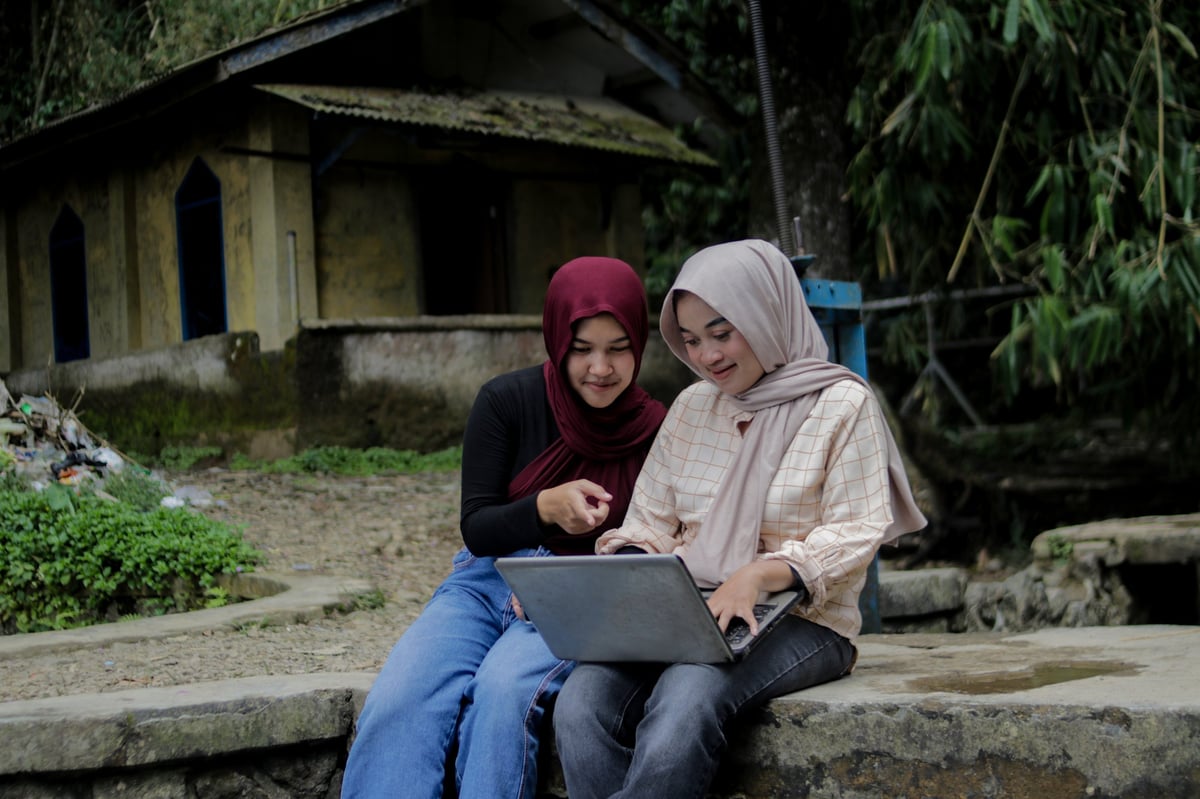Two Asian Muslim women in hijabs working together on a laptop outdoors