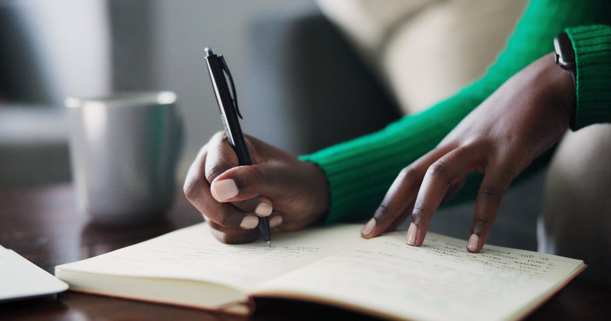Hands writing in a notebook on a cozy desk with a coffee cup